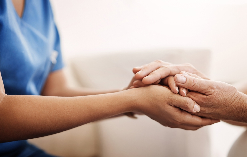 Support,,nurse,and,senior,woman,holding,hands,on,sofa,for